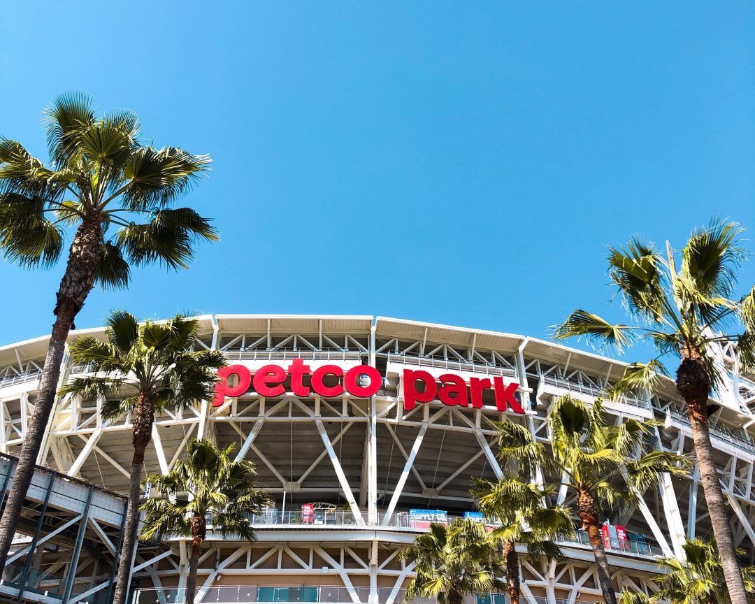 Palm trees frame the sign for Petco Park Stadium with a cloudless blue sky behind.