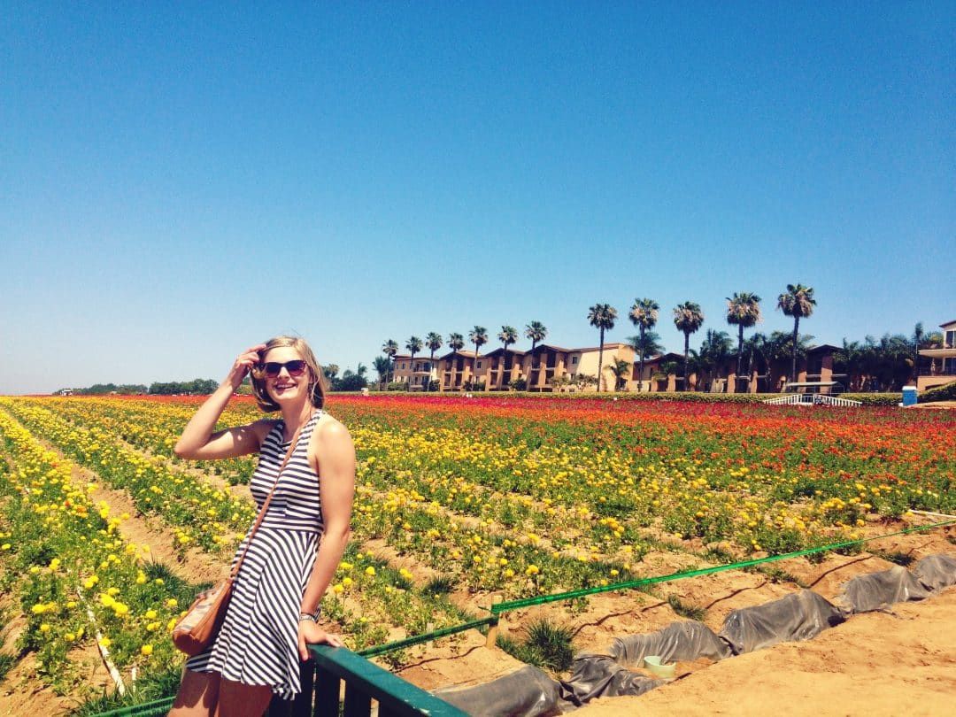 A young woman with short, light brown hair and a sundress, standing in front of the flower fields in Carlsbad, San Diego.