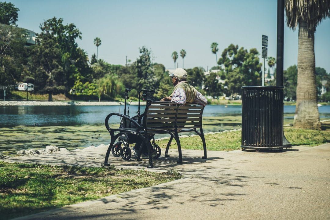 An elderly man sits on a bench and looks out at a pond in Echo Park.