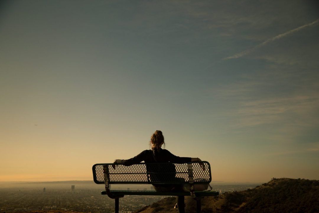 A woman sits on a bench at sunset and enjoys the view of the city at Runyon Canyon Park.