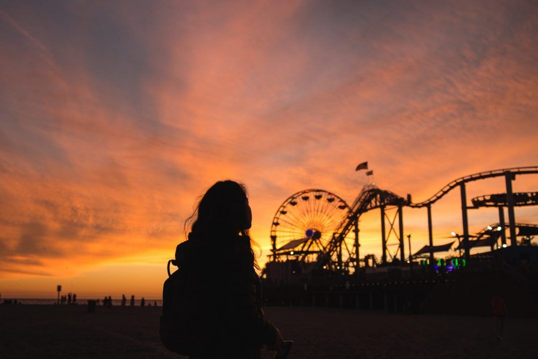 The silhouette of a young girl and amusement park rides at Santa Monica pier against a beautiful sunset.