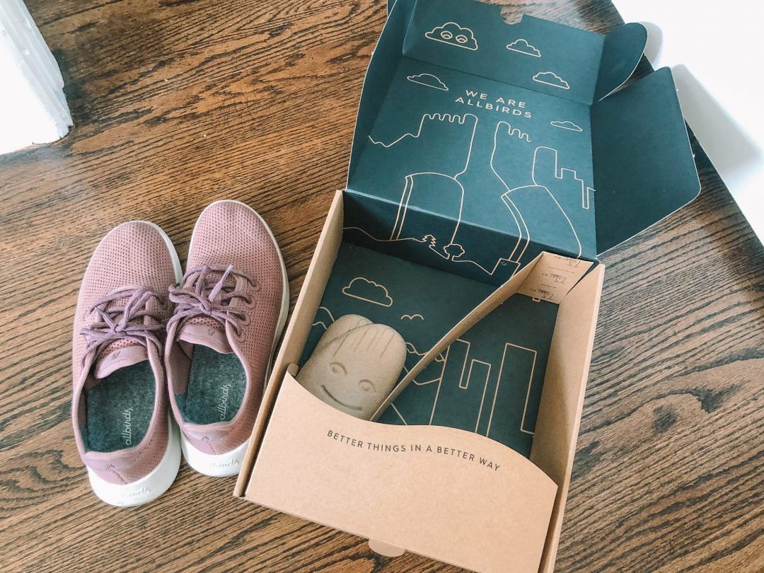 A pair of Allbirds tree runners in pink, sitting on a hardwood floor next to the shoebox they came in.