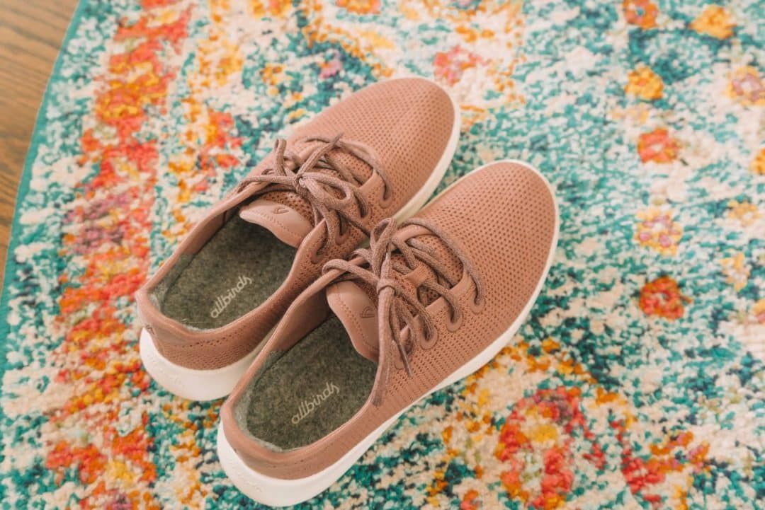 A pair of pink Allbirds tree runners sitting on a multicolored rug.