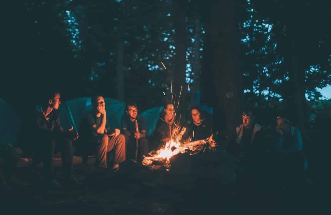 A group of campers hanging out around a fire at night. 