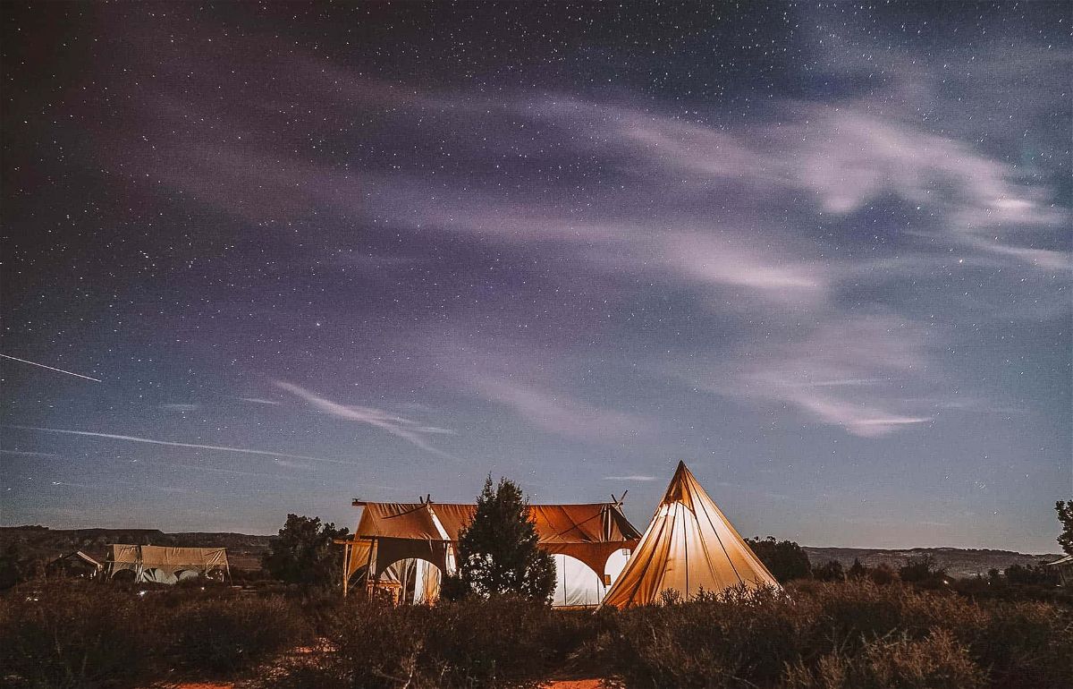Three large canvas tents glowing with light in a nighttime landscape.