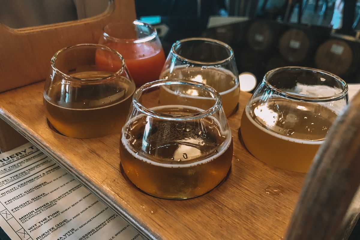 A set of five small glasses of different types of craft beers sitting in a wooden holder.
