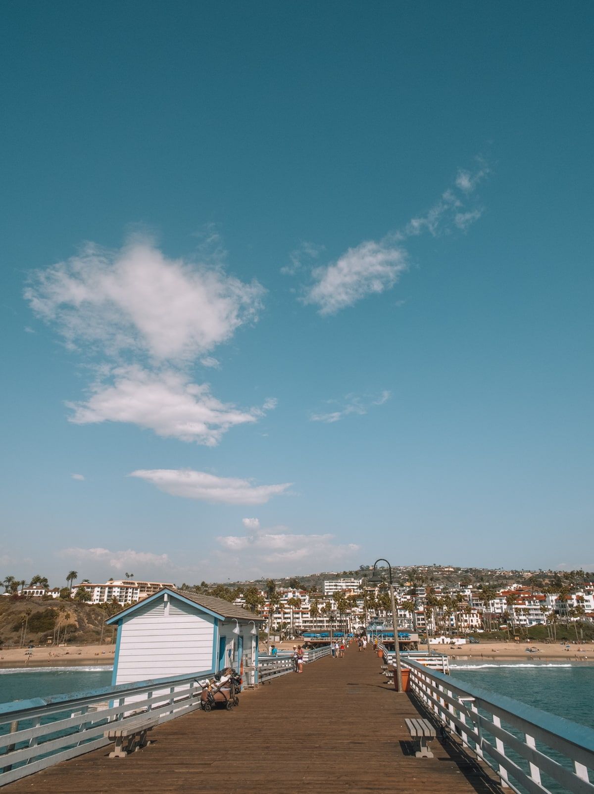 One of the best things to do in Orange County is go to the beach--shown here from the end of a long pier, with white condos dotting the hillside and a sunny sky above.