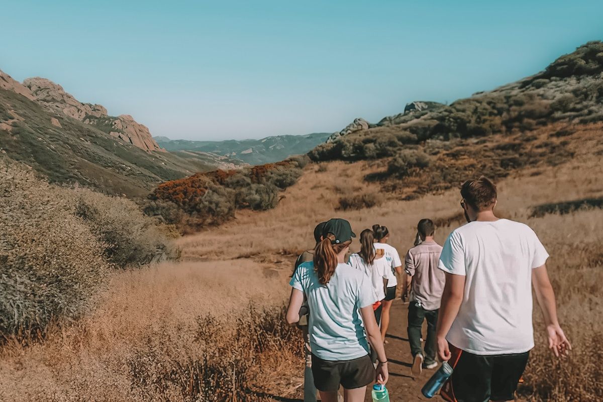 A group of people seen from behind as they hike on a trail through a dry, grassy valley at Circle X Ranch.
