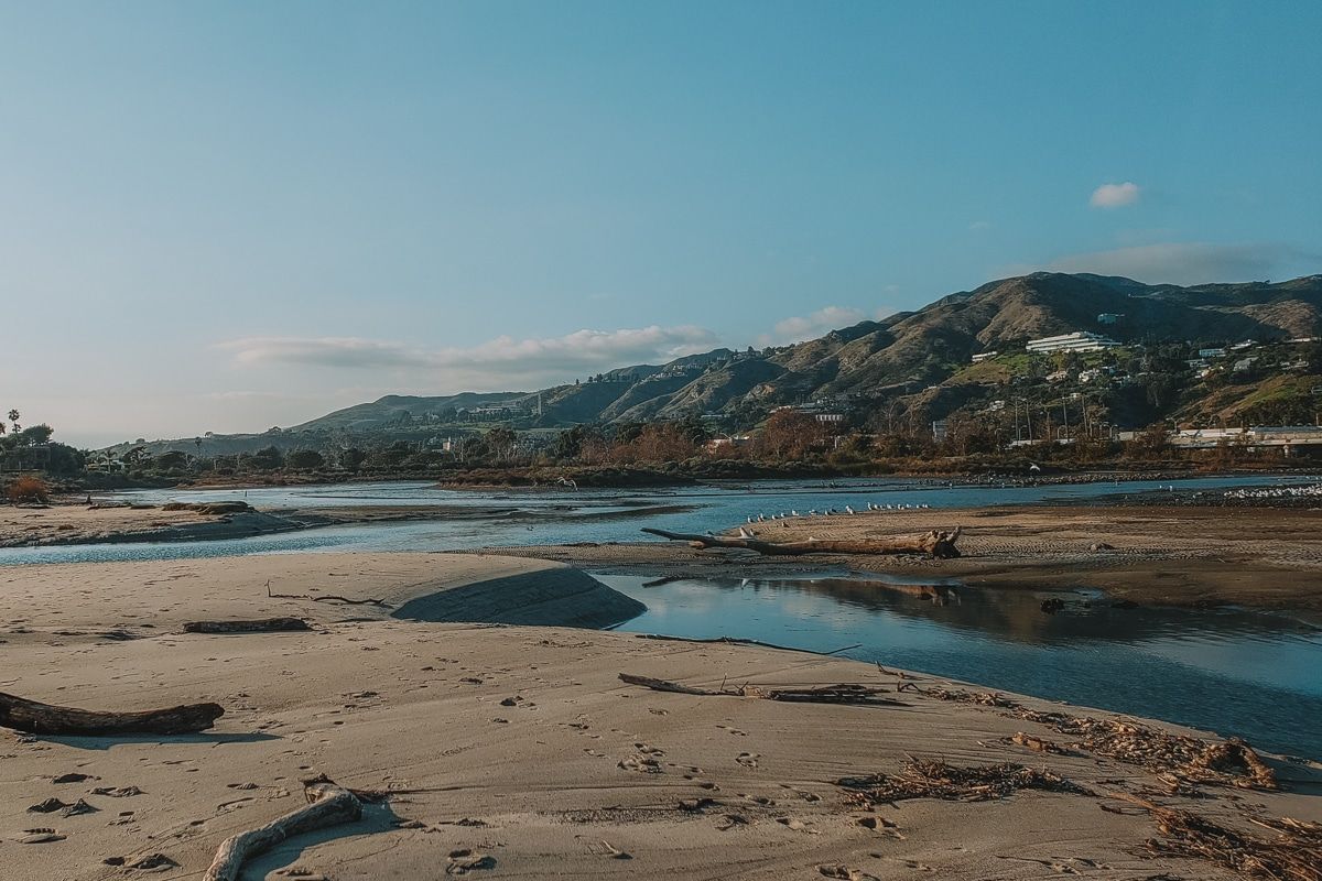 A view of sand banks and tide pools at Malibu Lagoon State Beach, with hills and blue sky in the background.