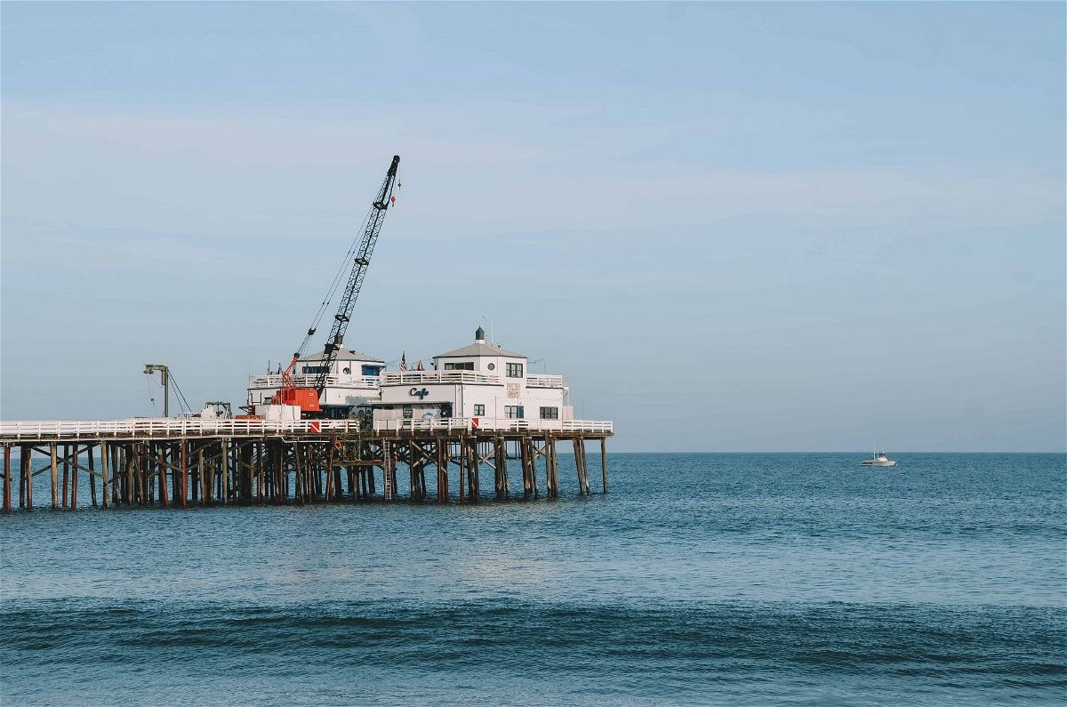 A pier sticking out into the ocean, with a white cafe and a crane on the tip of the pier.