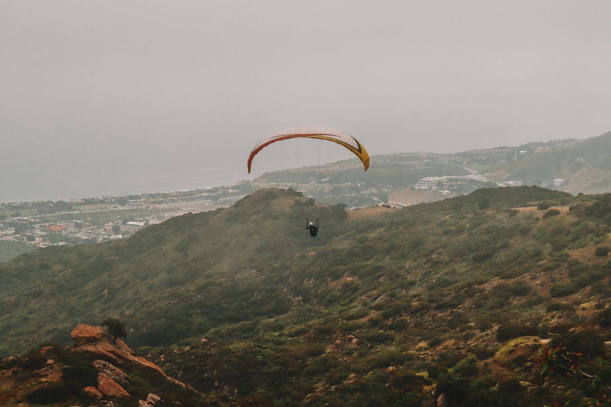 A person paraglides over California hills on a grey, overcast day.