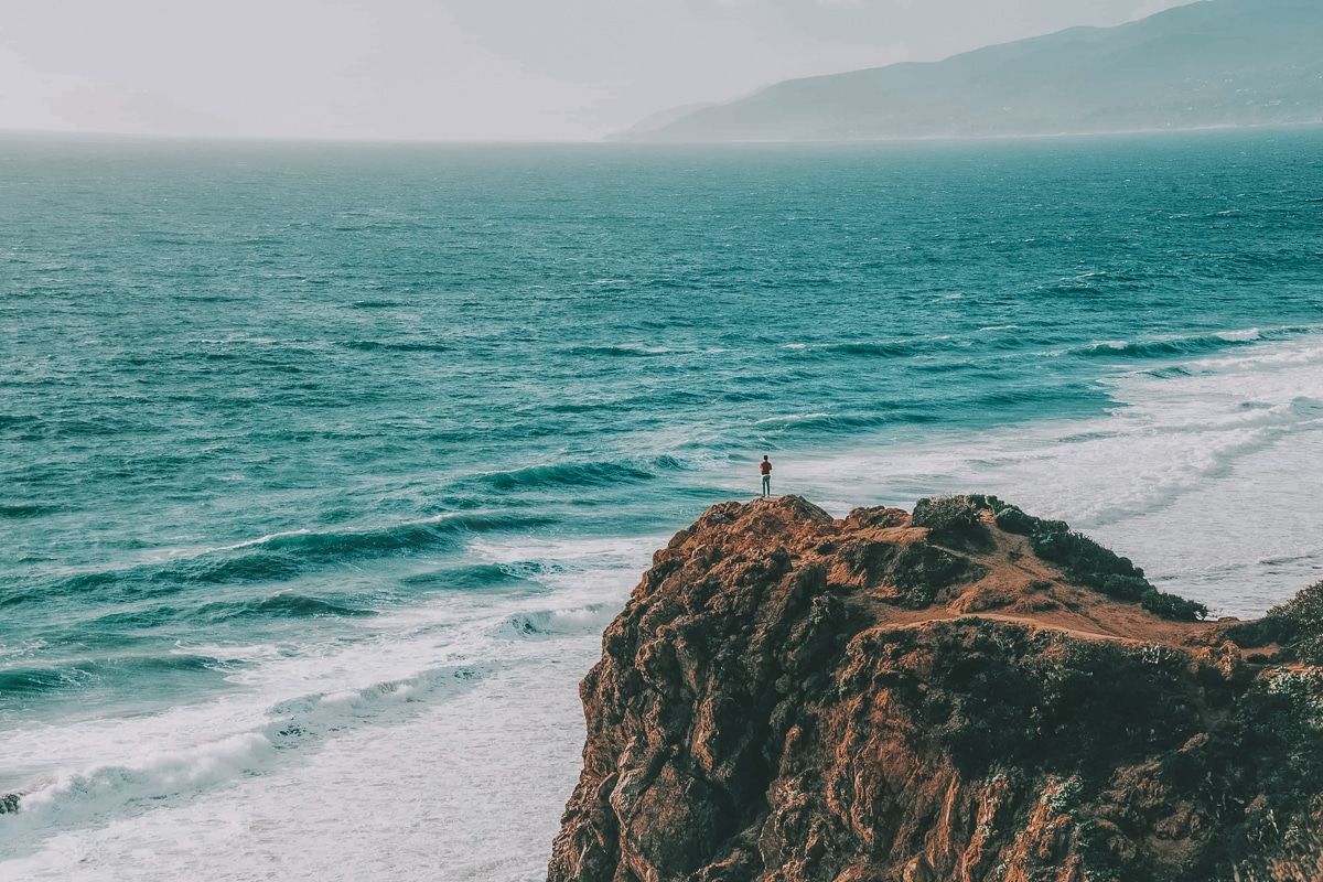 A small figure standing on a rock looking out at the ocean at Point Dume State Beach.