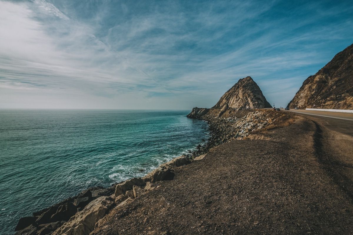 A view of the pebbly, rocky, Point Mugu State Park, with a partly cloudy sky in the background.