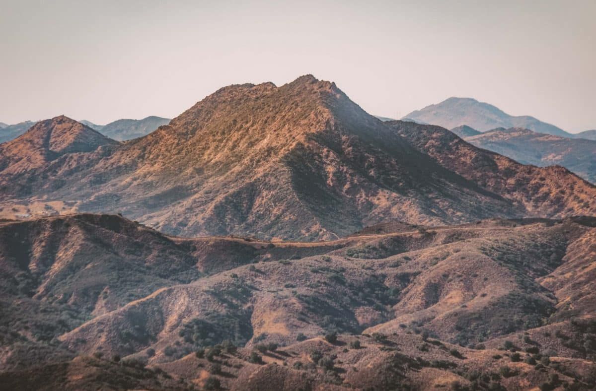 Scenic overlook of the brown peaks of Calabasas with the Santa Monica Mountains in the background and a hazy sky beyond.