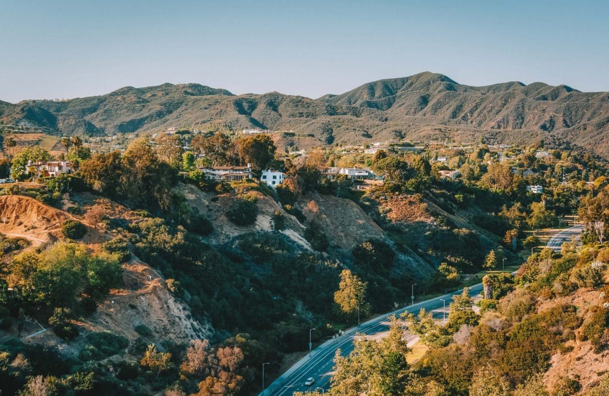 An overhead view of a road running through the Temescal Canyon in Pacific Palisades, California, with houses and sparse trees dotting the hillside.