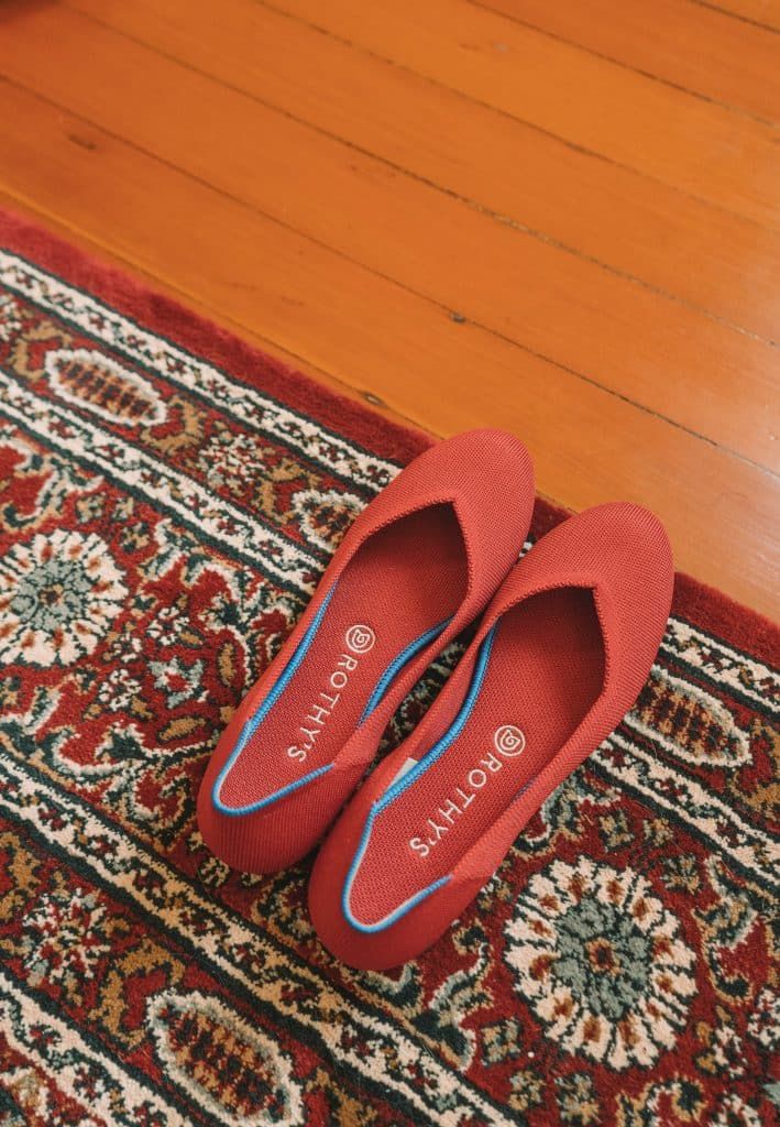 Rothy's Shoes Review: a pair of red Rothy's flats sitting on the edge of a red oriental rug, with a hardwood floor visible under the rug.