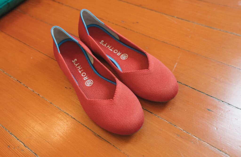 A pair of red Rothy's flats sitting on a hardwood floor.