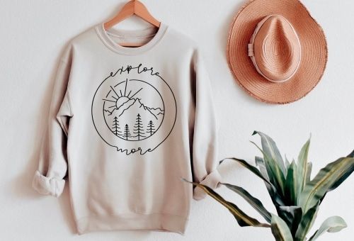 Explore More Sweatshirt next to a hanging hat and plant.
