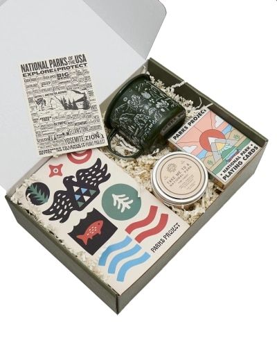 The inside of the National Park Gift Box with playing cards, a journal, a mug, a candle, and a checklist postcard. 