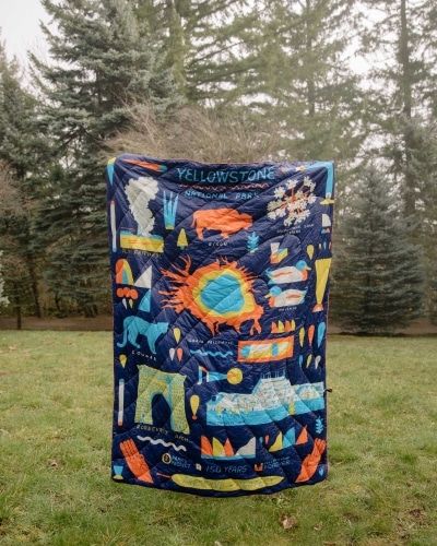 The Yellowstone Rumpl Puff Blanket being held up by someone outside on the grass.