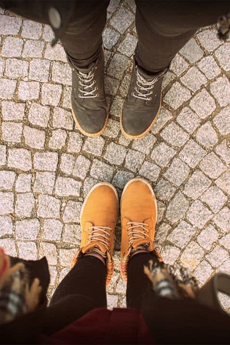 Two pairs of feet wearing waterproof shoes for walking standing on cobblestone and facing each other.