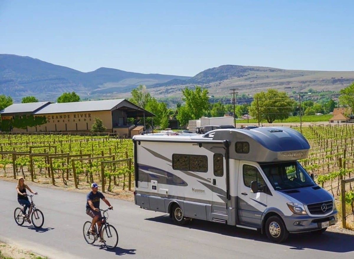 An RV driving through a vineyard with two bikers on the side of the road to signify a Harvest Hosts Membership.