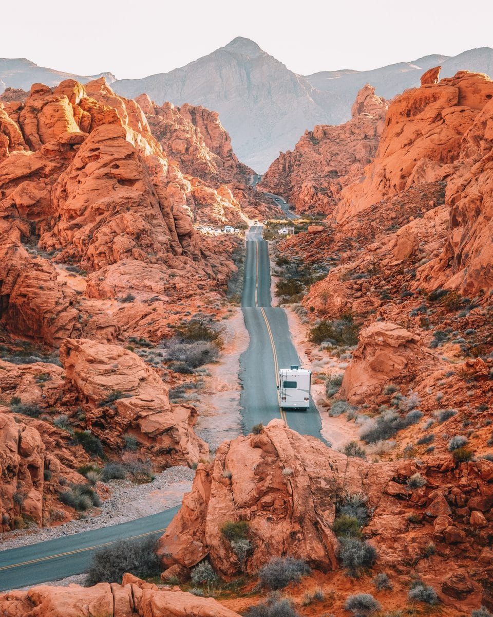 A white RV on a lonesome highway in the southwest USA with reddish-orange rocks all around.