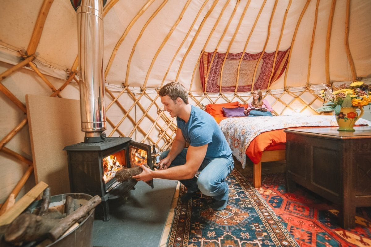 A man putting a log into one of the best tent stoves while glamping in a canvas tent with a stove jack.