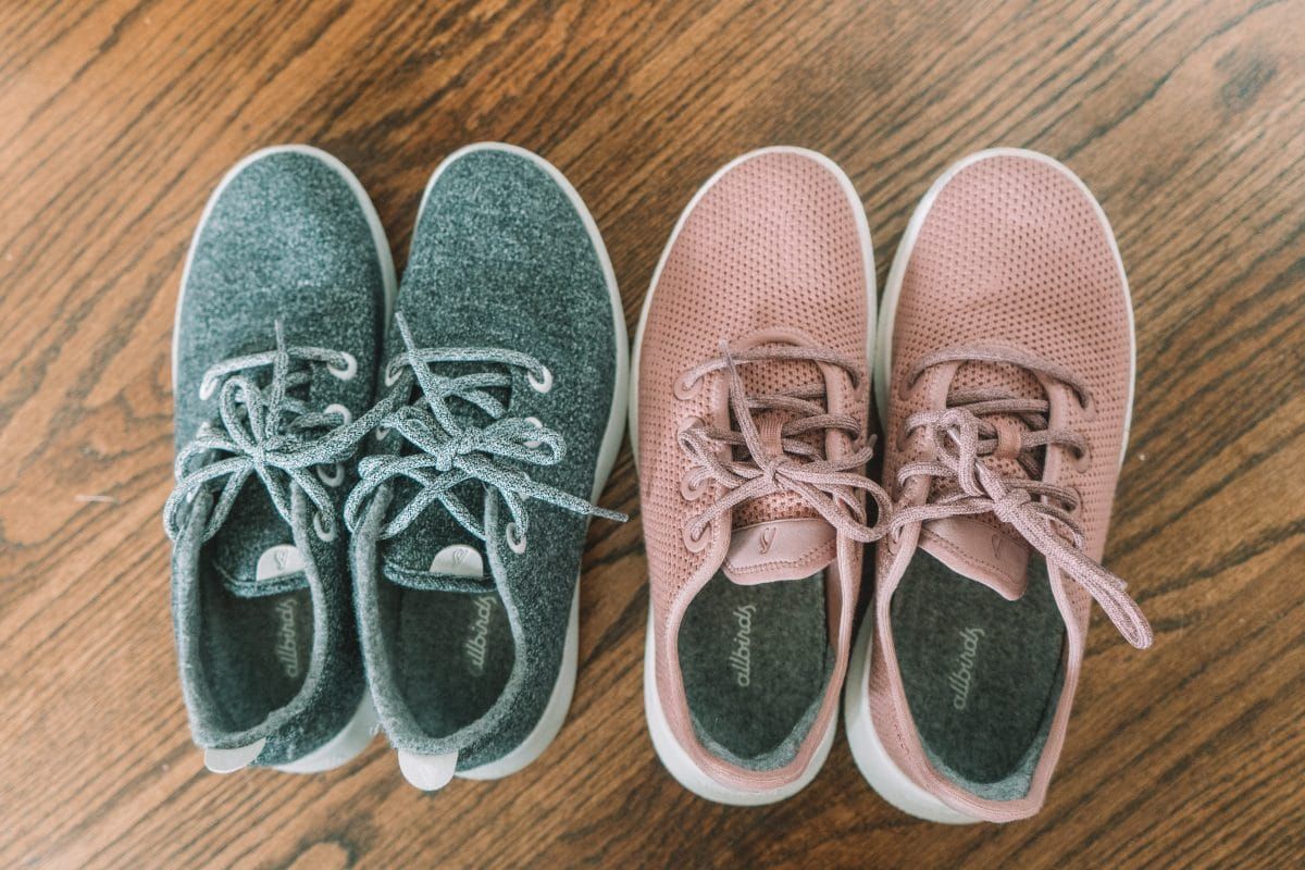 A pair of grey Allbirds sneakers sitting next to a pair of pink Allbirds sneakers on a hardwood floor.
