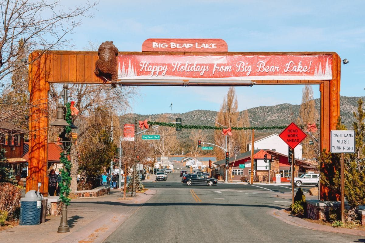 A sunny day looking down a main street in Big Bear Lake at Christmas, with a banner overhead wishing Happy Holidays.
