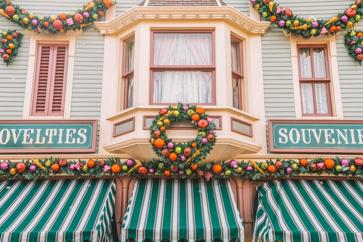Wreaths decorate the facade of a green building with green striped awning and a sign that says, "Souvenirs," during Christmas in Disneyland.