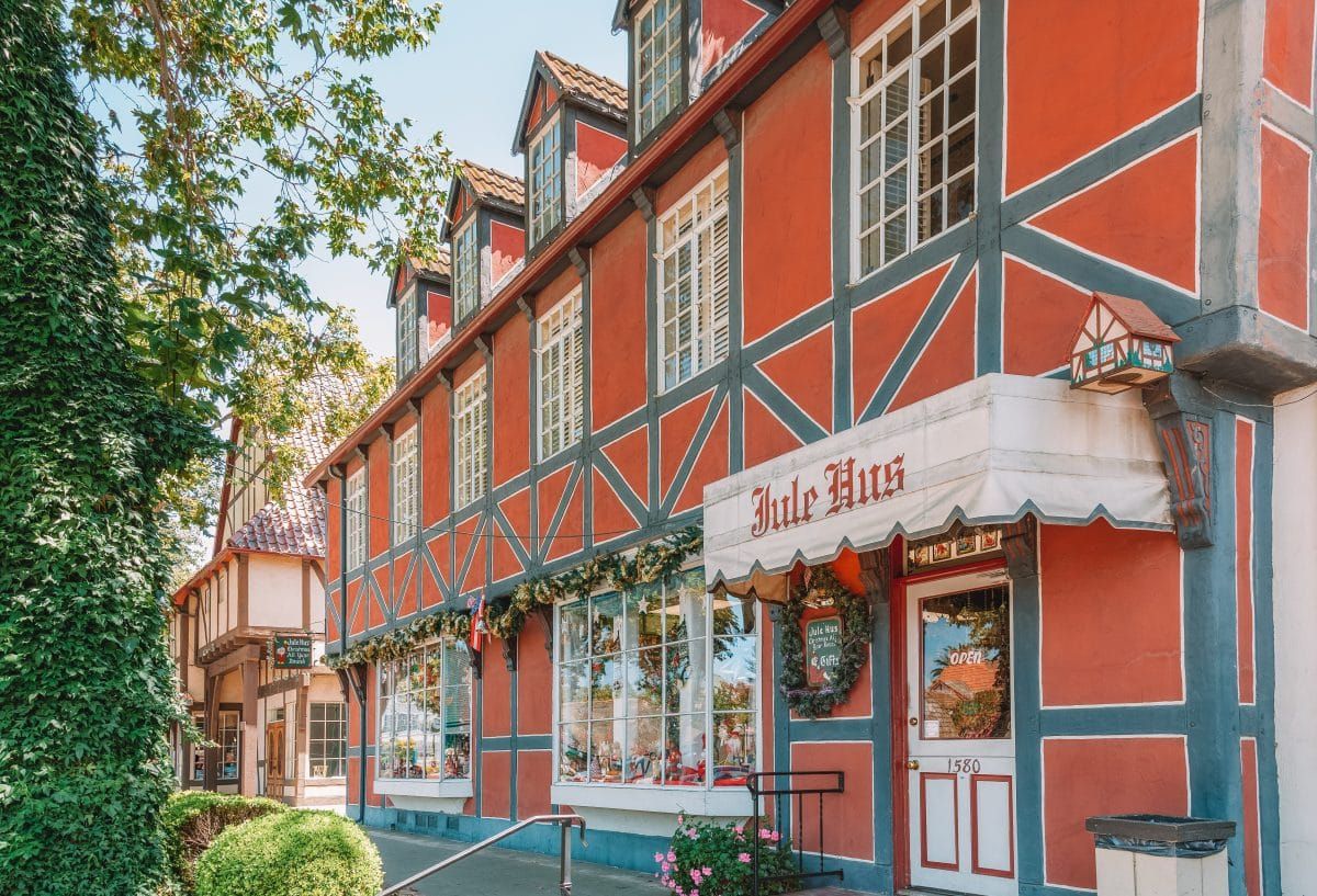 A red, storybook -style building in Solvang, California, with a storefront in the foreground bearing a white awning with red, old English text on it.