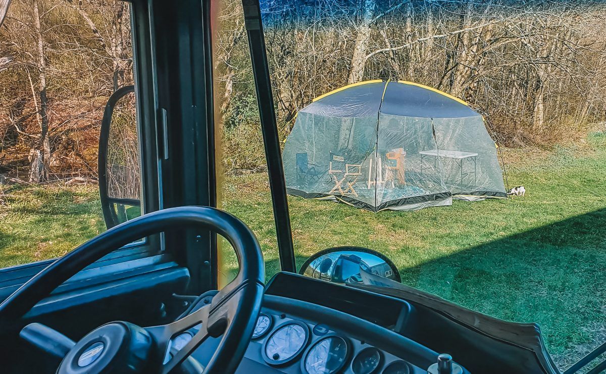 A view looking out from a tractor driver's seat of a screen house tent pitched on a lawn with leafless trees behind it.