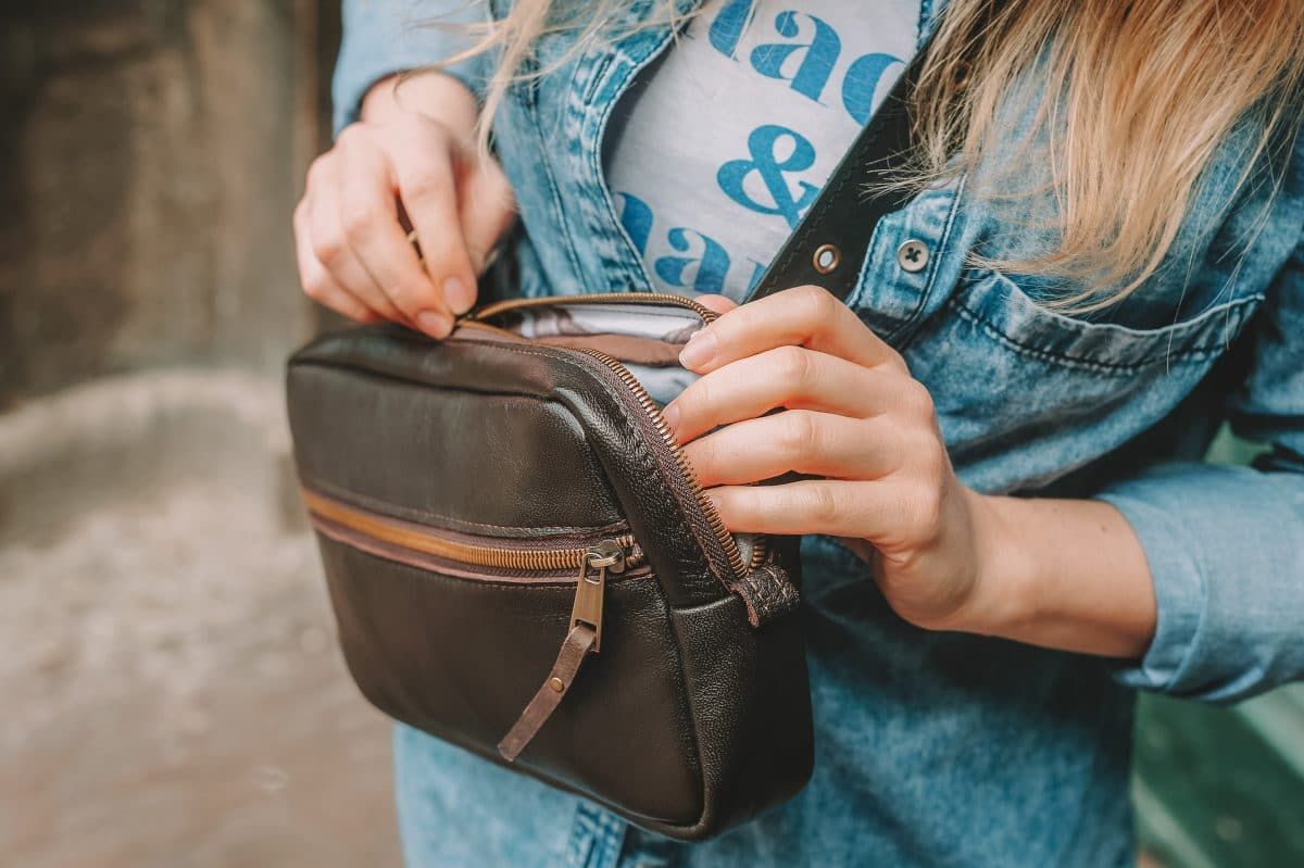 Close up of a blonde woman unzipping a small, brown leather purse.