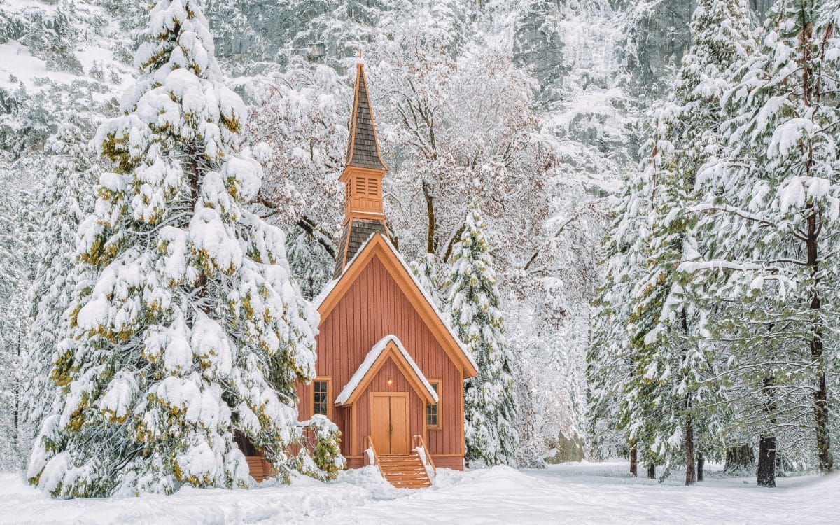 A brown wooden church nestled in a snowy forest scene in Yosemite.