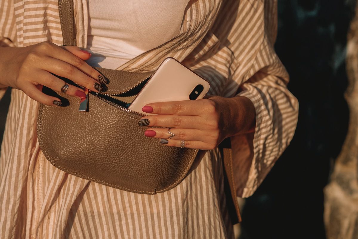 Close up of a woman with painted nails holding a small leather purse close to her torso.
