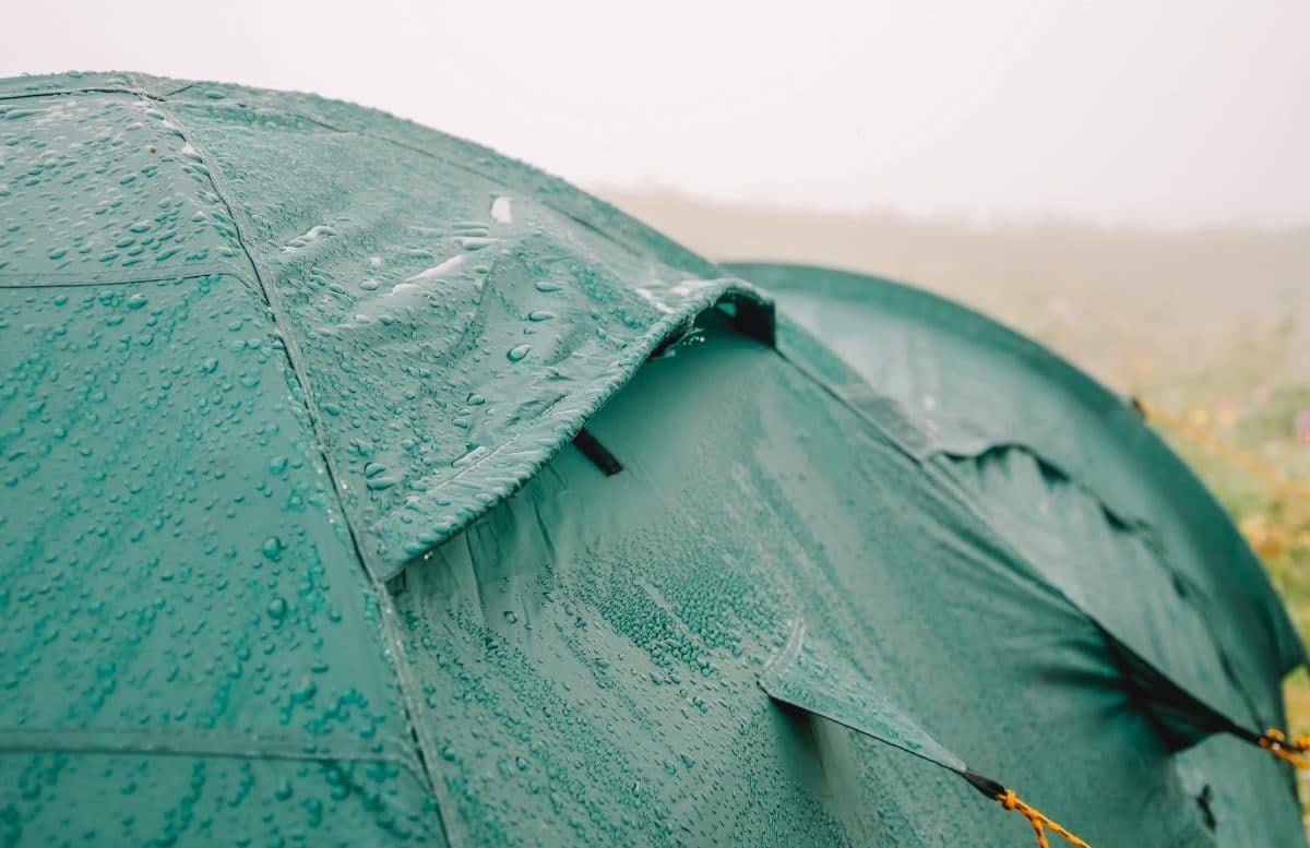 A close-up of water beading on a dark green waterproof tent rainfly.