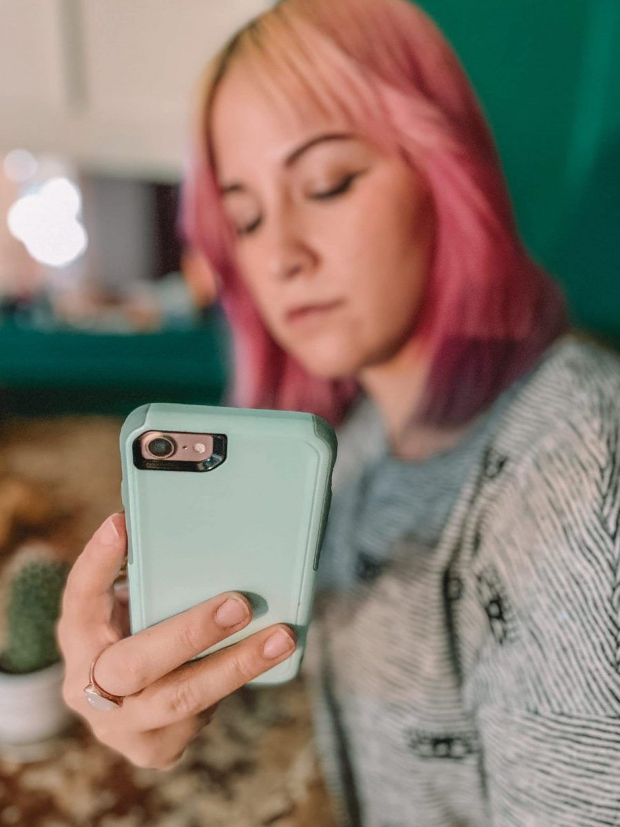 A pink-haired woman in soft focus holding a light blue phone case in the foreground.