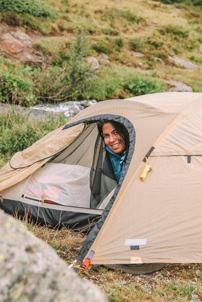 A smiling dark-haired woman peeks out of one of the best waterproof tents, a brown tent with raindrops on it.