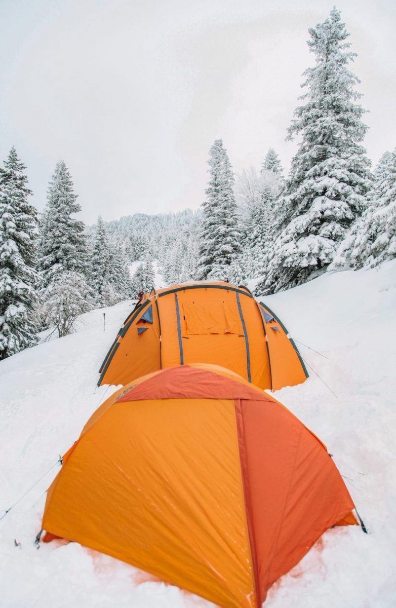 Two bright orange tents set up in deep snow.