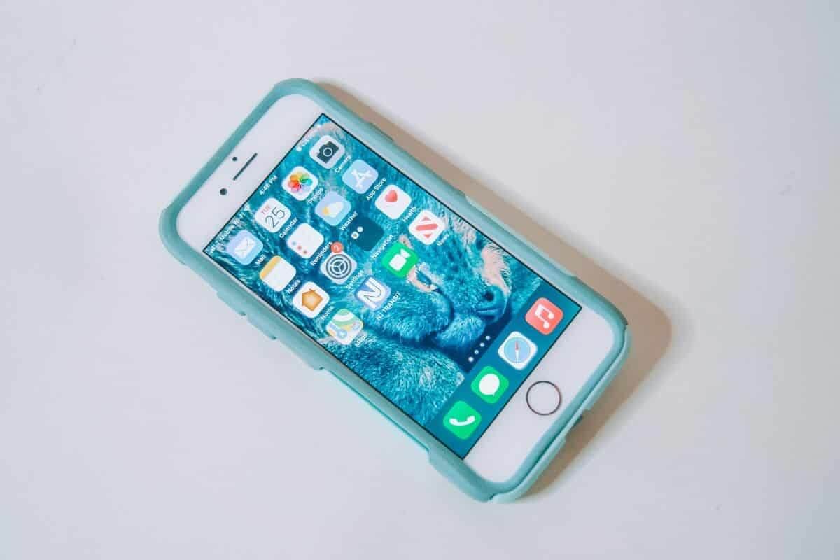 An iPhone in a teal Otterbox Commuter phone case, sitting on a white background, with the home screen facing up.