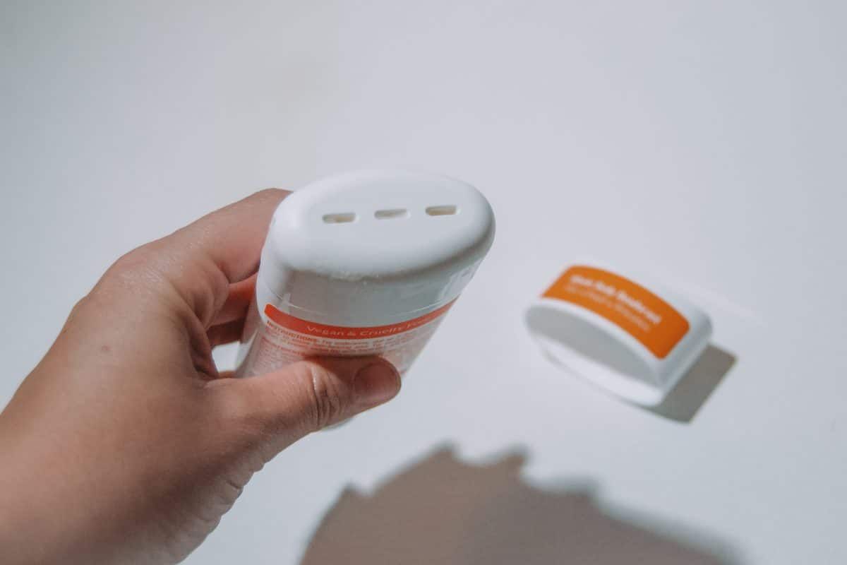 A hand holding an uncapped Lume cream stick on a white background.