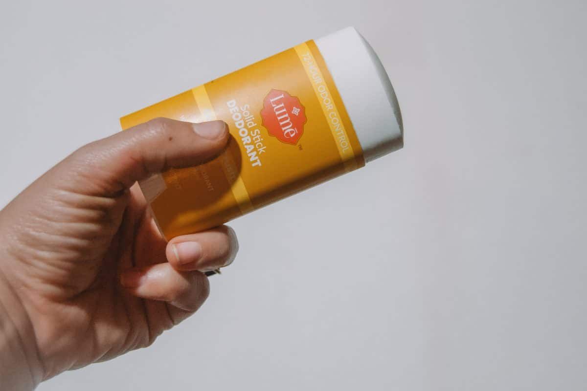 A hand holing up a solid stick of Lume deodorant on a white background.