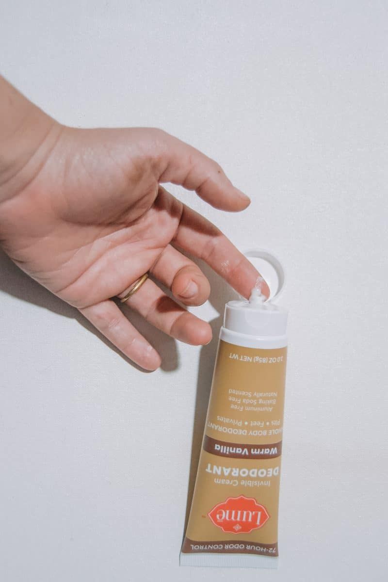 A hand touching a squeeze of Lume Natural Deodorant from the Warm Vanilla tube, on a white background.