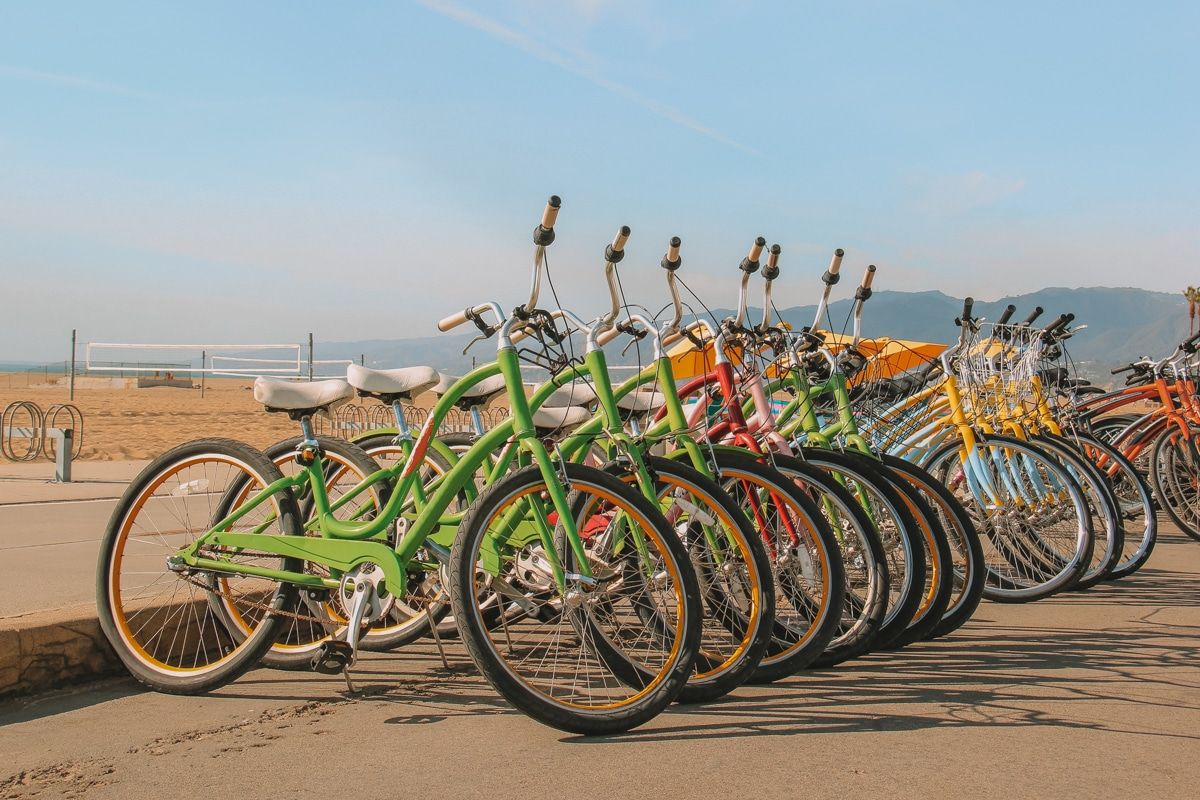 A row of brightly colored bikes parked in a row next to the beach on a sunny day.