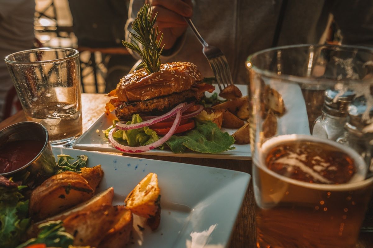 A close-up of a restaurant table laden  with burgers and pints of draft beer.