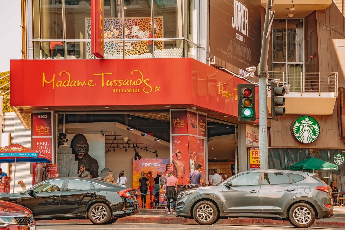 The busy front entrance and red sign of Madame Tussaud's Hollywood, with a Starbucks visible next door.
