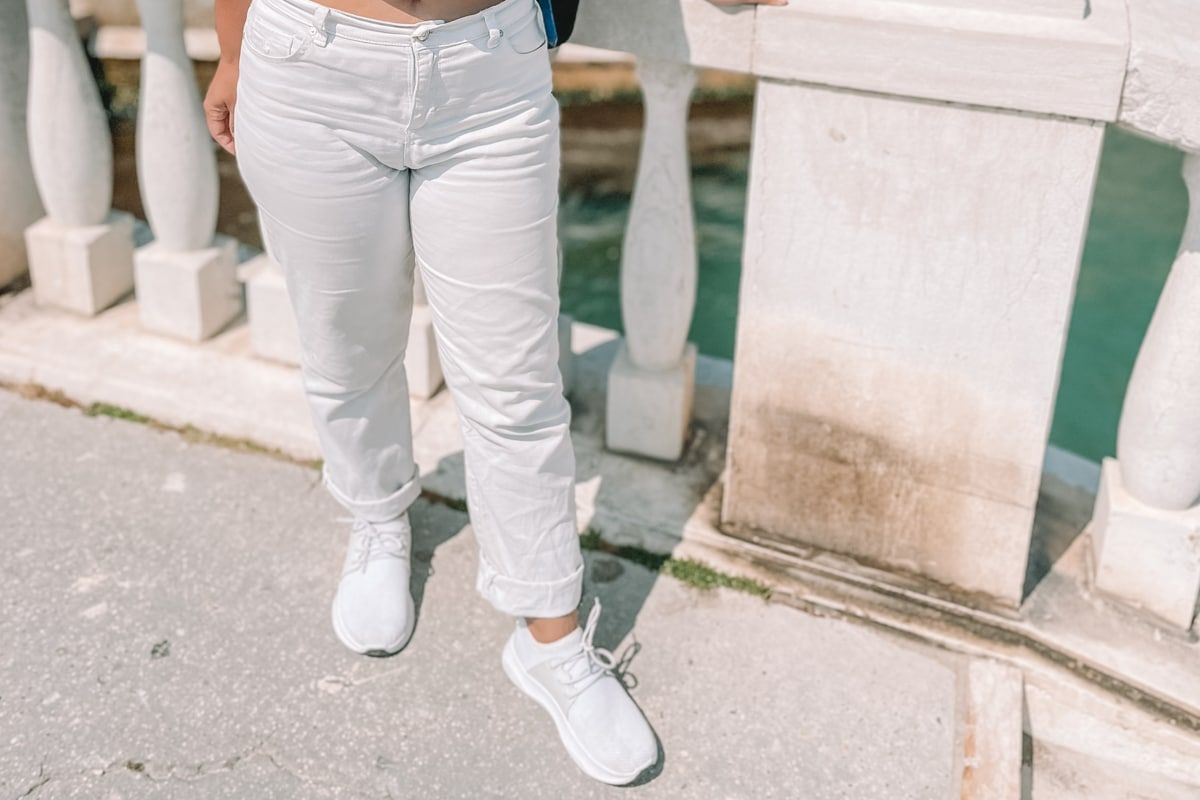 A woman white jeans and white Vessi shoes seen from the waist down stands on a bridge in Venice.