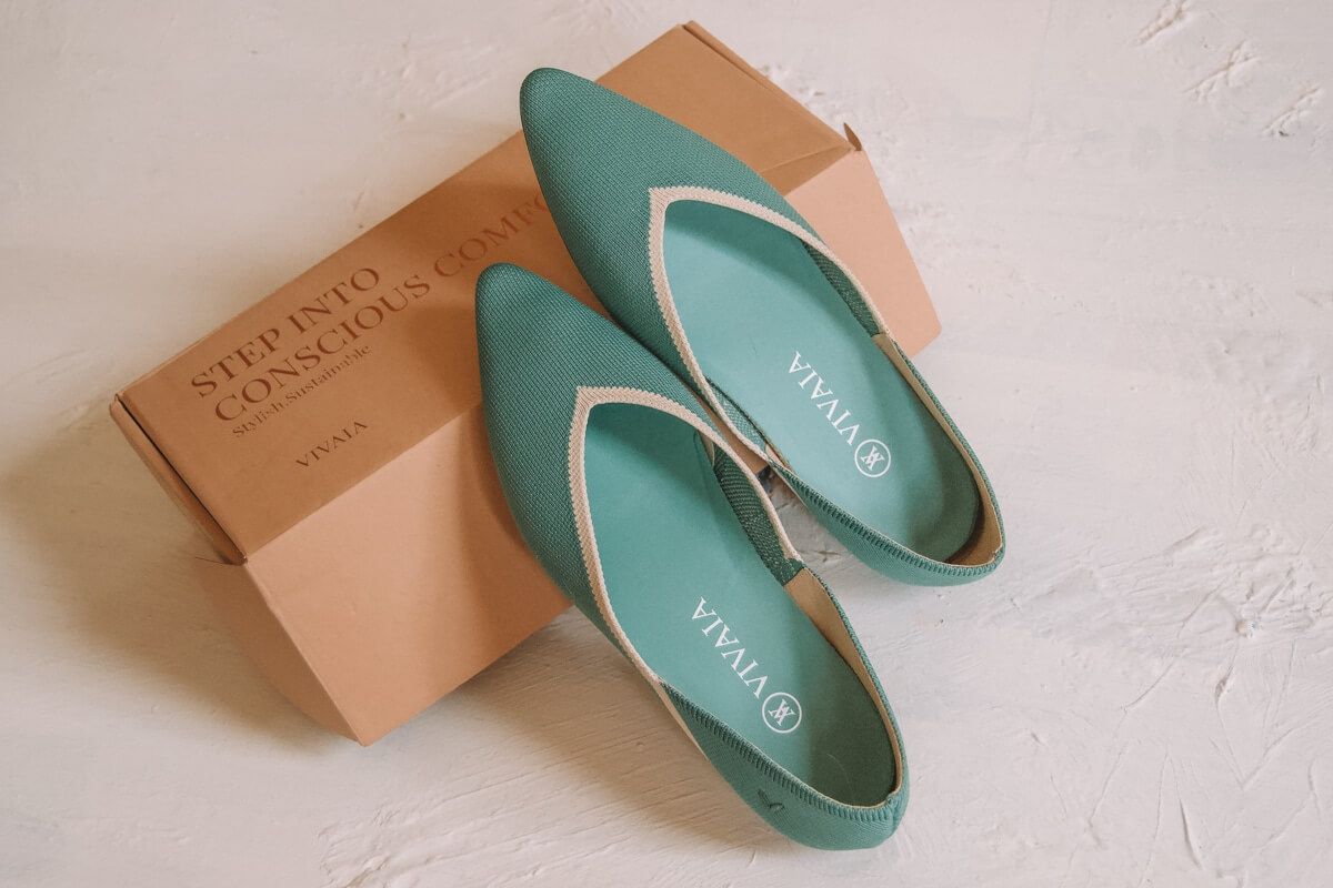 Teal Vivaia Vienna Flats with pointed toes and cream-colored trip, leaning up against the shoe box.