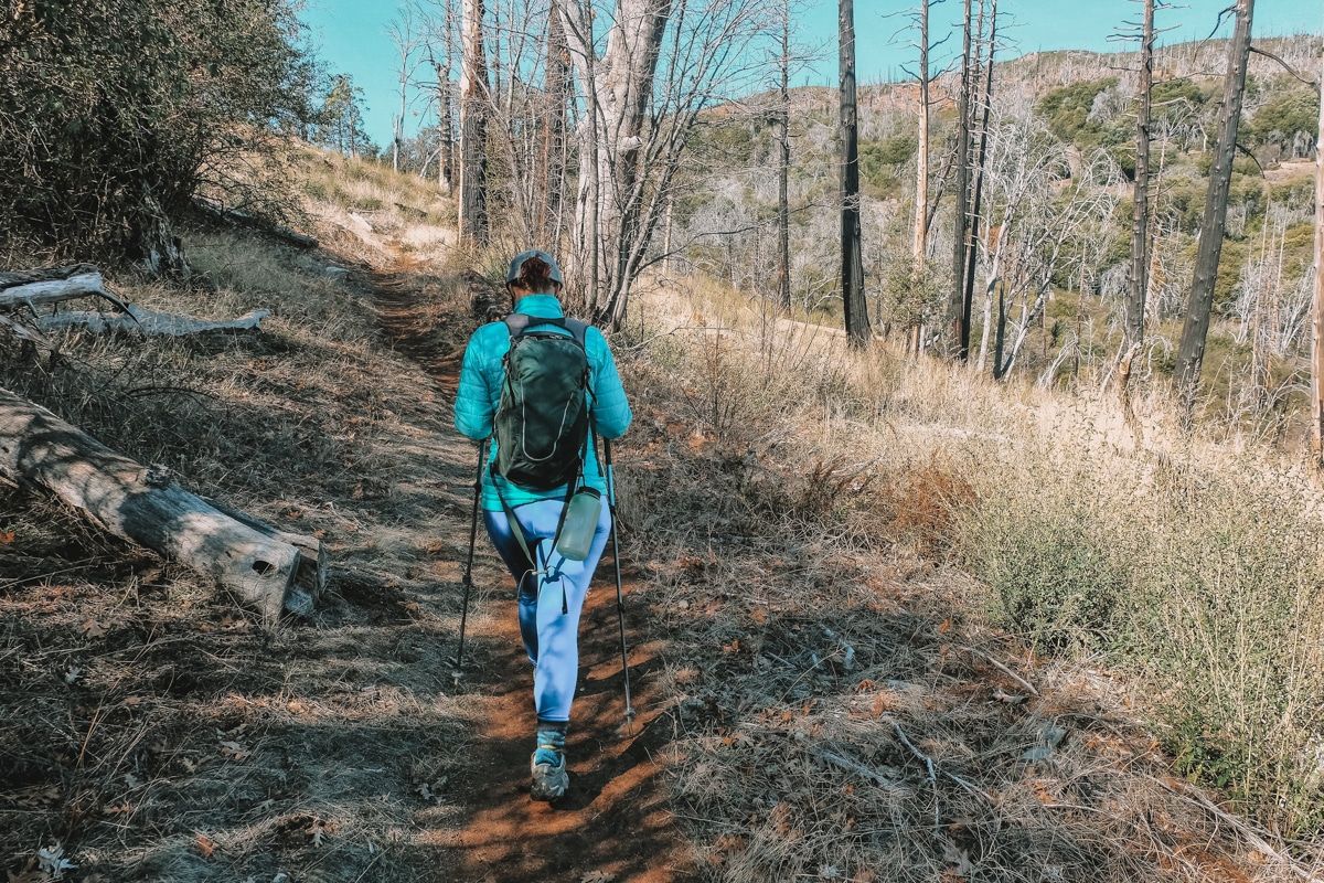 A woman in bright blue hiking clothes on a path lined with dry grass in Cuyamaca Park.